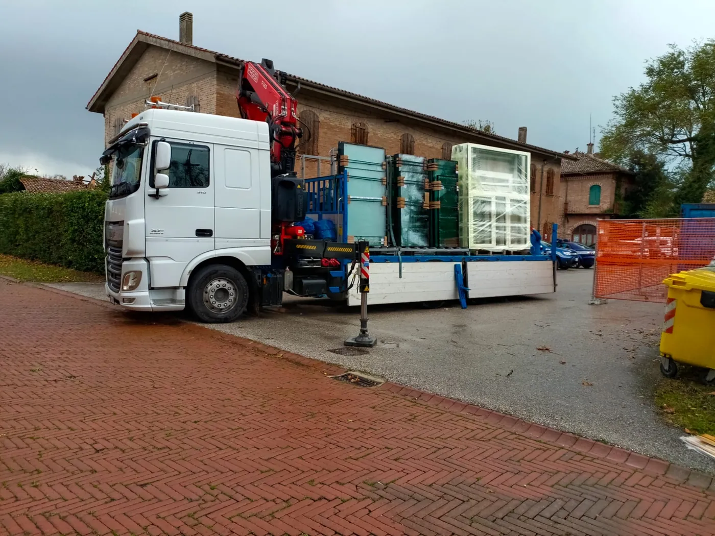 Camion con gru carico di serramenti davanti all'edificio